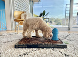 Bark potty pad with curly-haired dog sniffing near a blue fire hydrant toy in a bright indoor setting